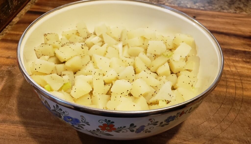 Cubed potatoes in a bowl with celery seed and diced celery for a classic old-fashioned potato salad with a creamy cooked dressing