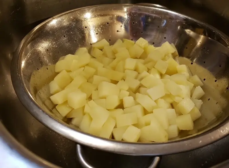 Freshly boiled potatoes draining in a colander, ready for a classic old-fashioned potato salad with creamy cooked dressing