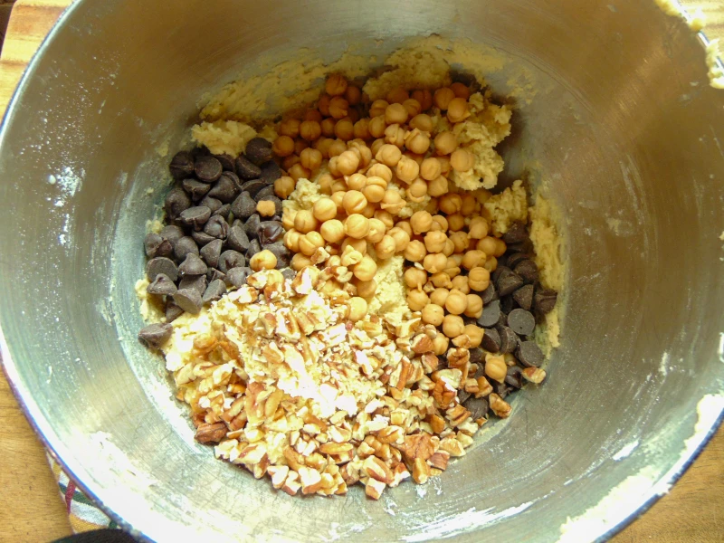 chocolate chips, caramel bits and pecans being folded into cookie dough